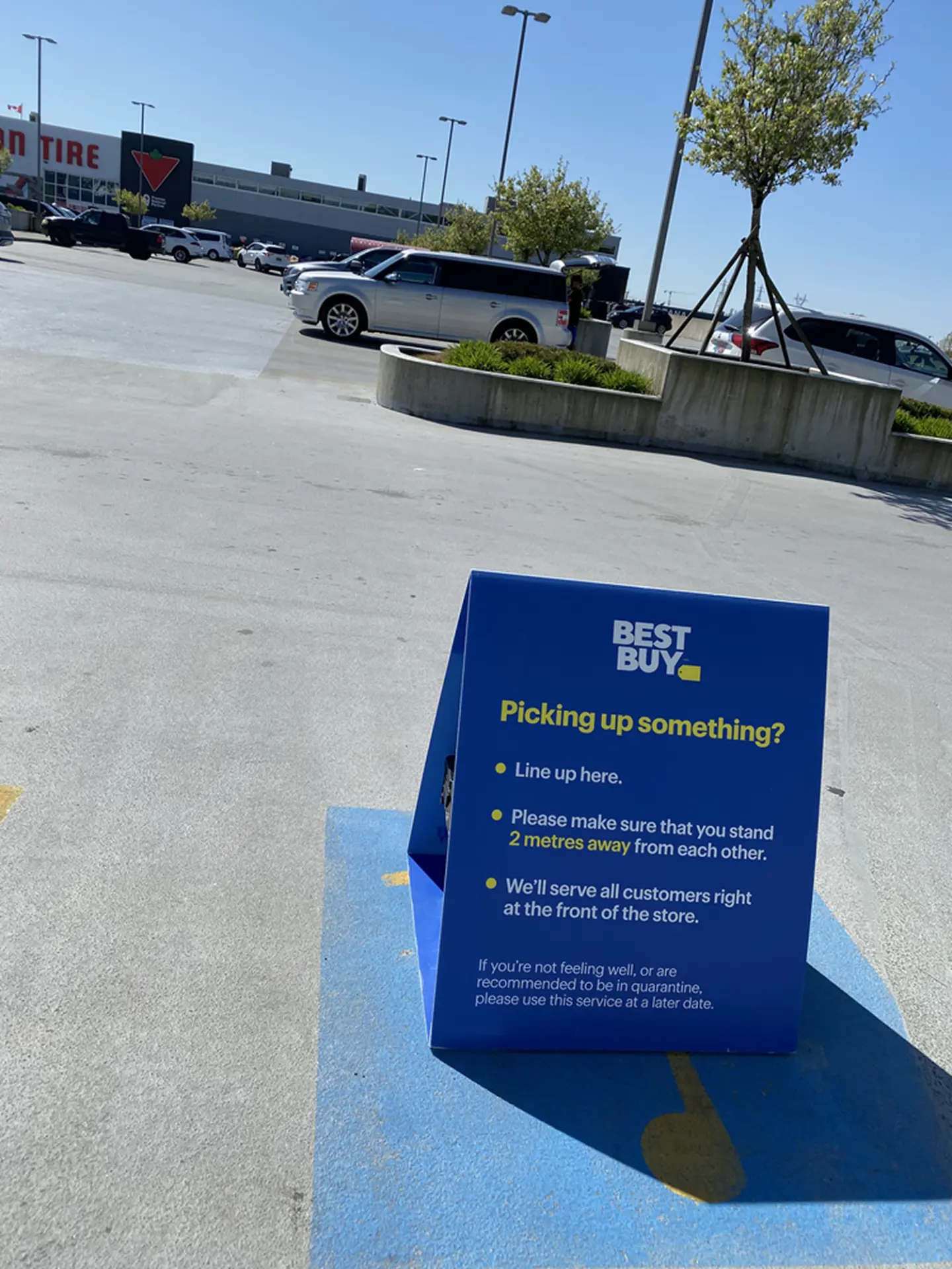 Blue Best Buy sandwich board sign in an open parking lot telling customers where to line up and to keep a two-metre distance
