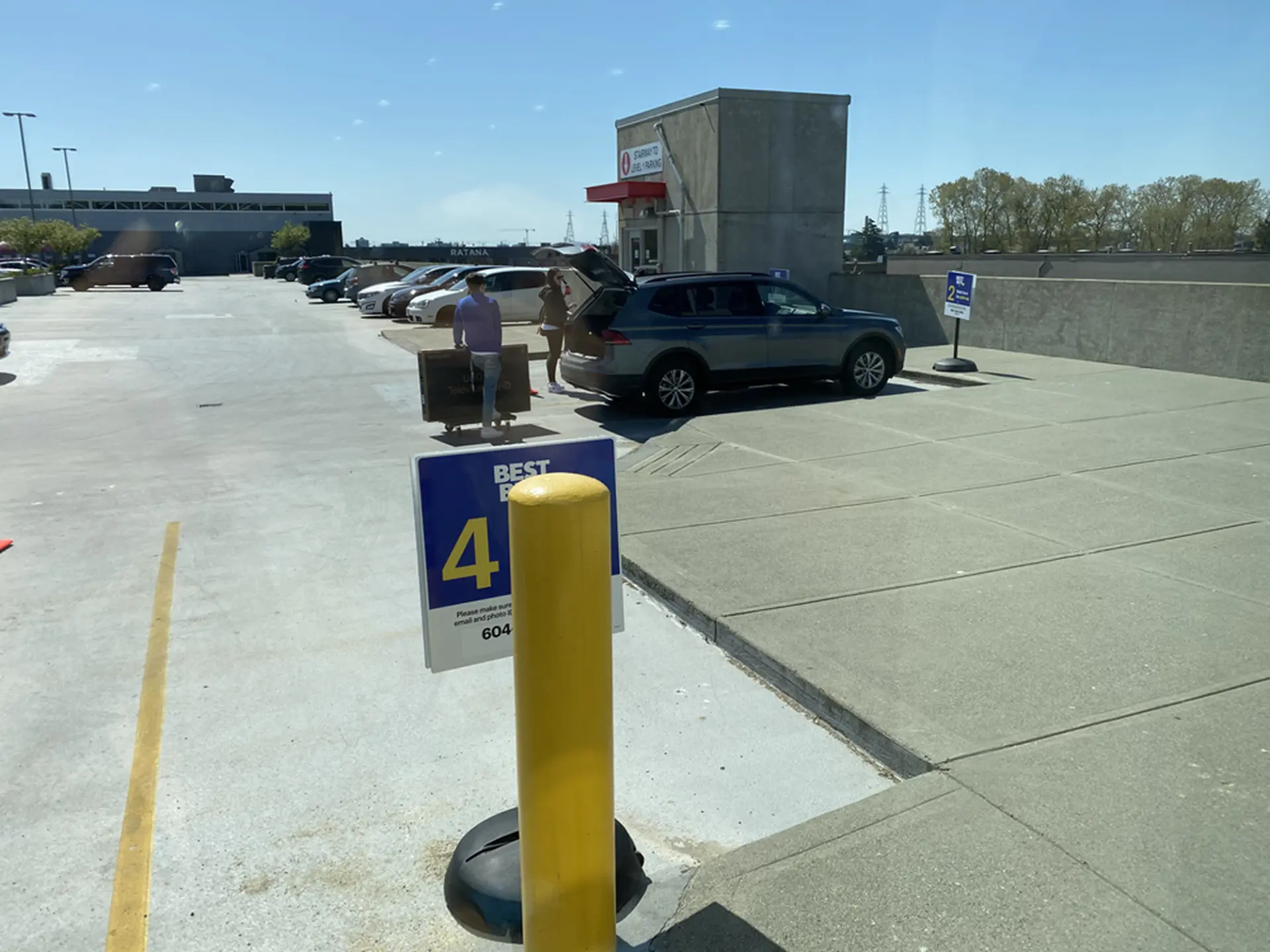 Customers loading a large boxed television into the open hatchback of an SUV in a marked curbside pickup stall
